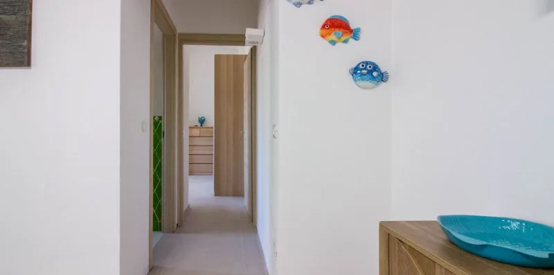 Un pasillo luminoso conduce a una habitación, con un mueble de madera y un lavabo azul en primer plano.