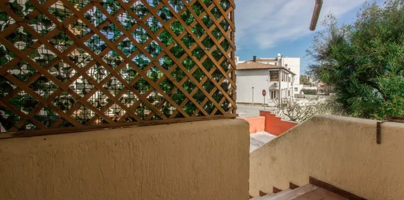Una terraza da a edificios cercanos, con una celosía de madera y vegetación frondosa.