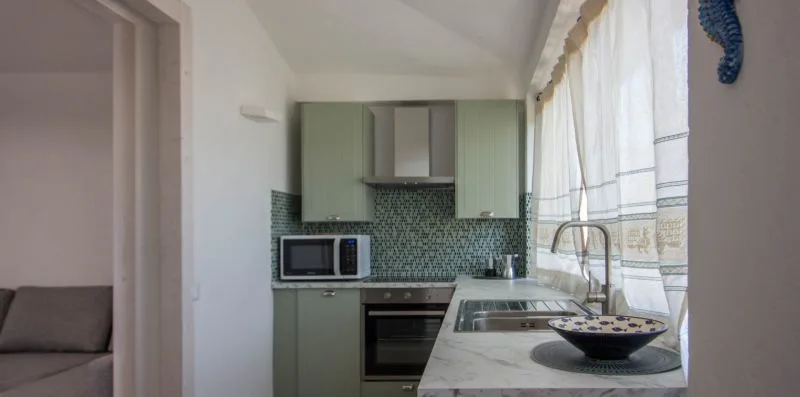 Una cocina con gabinetes verdes, un salpicadero de azulejos y una encimera junto a la ventana.
