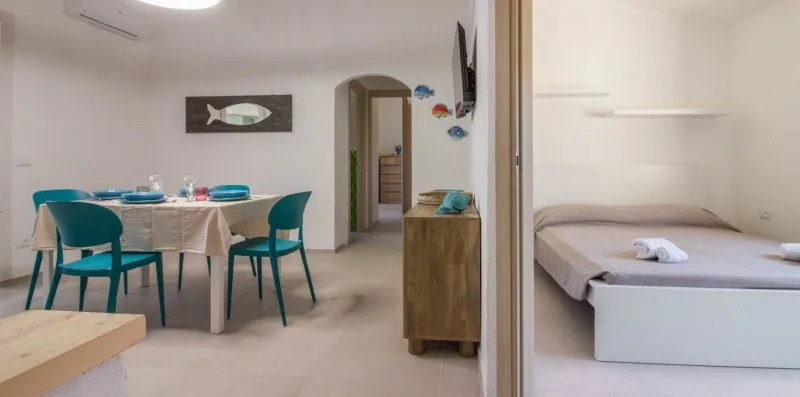 Un comedor con asientos verde azulado junto a un dormitorio con cama.