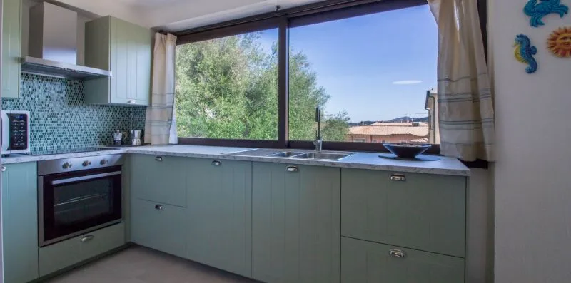 Una cocina con muebles claros, un salpicadero de azulejos y una ventana amplia.