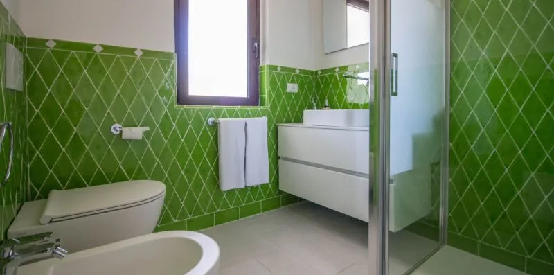 Un baño con paredes de azulejos verdes, lavabo, inodoro y ducha de vidrio.