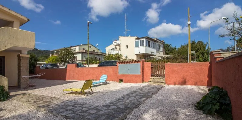 Un patio exterior pavimentado con un muro rojo bajo y una puerta de madera.