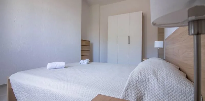 Un dormitorio con una cama grande, ropa de cama blanca y un armario.