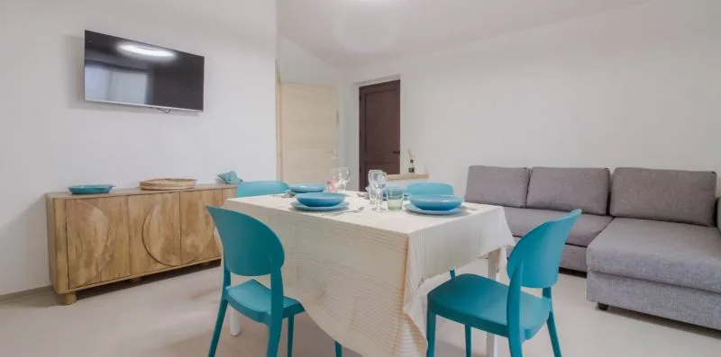 Comedor con una mesa y sillas turquesas junto a una zona de asientos grises.