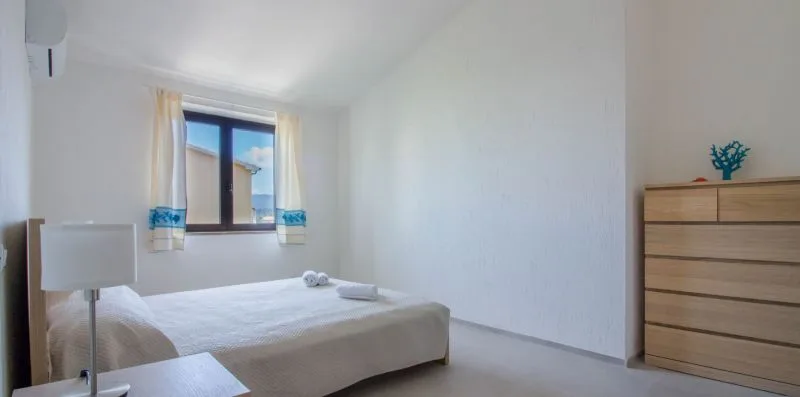 Un dormitorio luminoso con una cama bajo una ventana y una cómoda de madera.