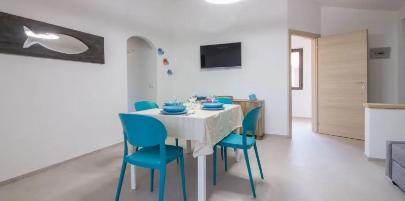 Un comedor con la mesa puesta, sillas azules y un televisor en la pared.
