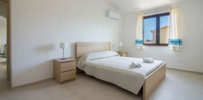 Un dormitorio luminoso con una cama tendida y una ventana con cortinas.
