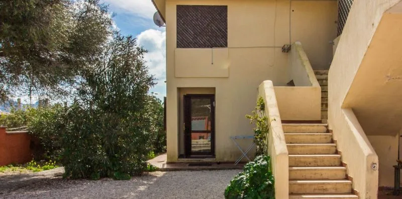 Una escalera exterior junto a un edificio beige, con un árbol frondoso cerca.
