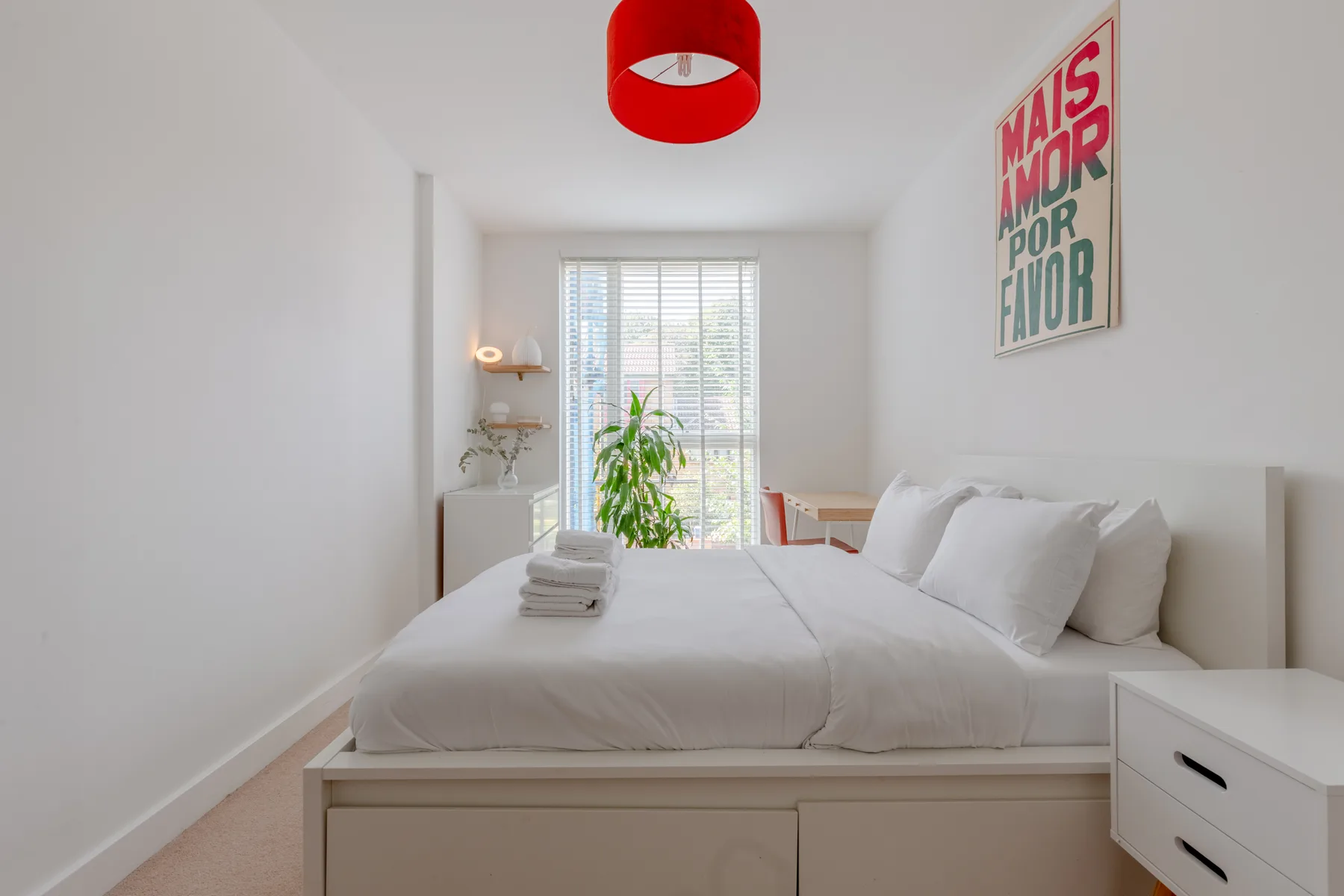 Un dormitorio luminoso con una cama tendida y una ventana con persianas.