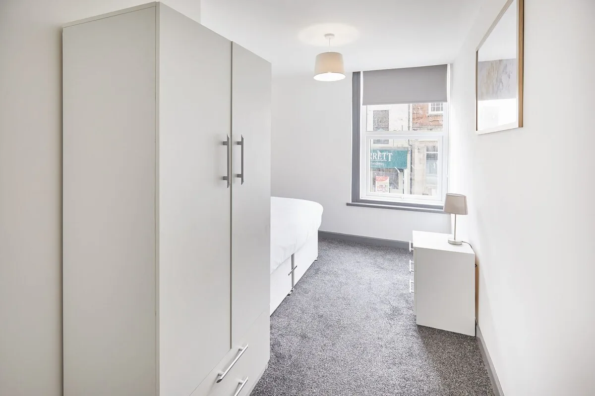 A bedroom with a bed, wardrobe, and window overlooking nearby buildings.