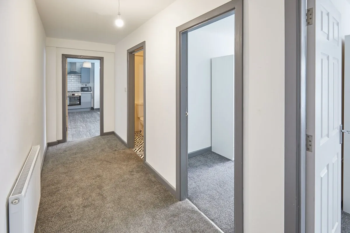 A carpeted hallway connects several doorways, with a kitchen visible at the far end.