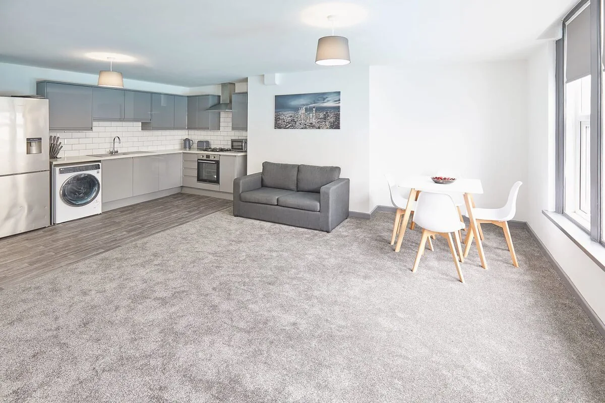 An open-plan living area with a kitchen, gray seating, and a dining table.