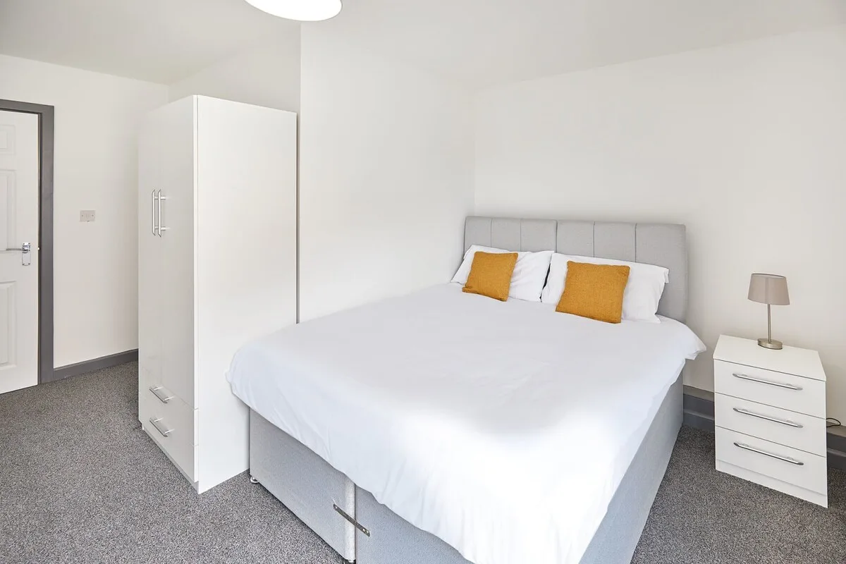 A bright bedroom with a neatly made bed and two bedside drawers.