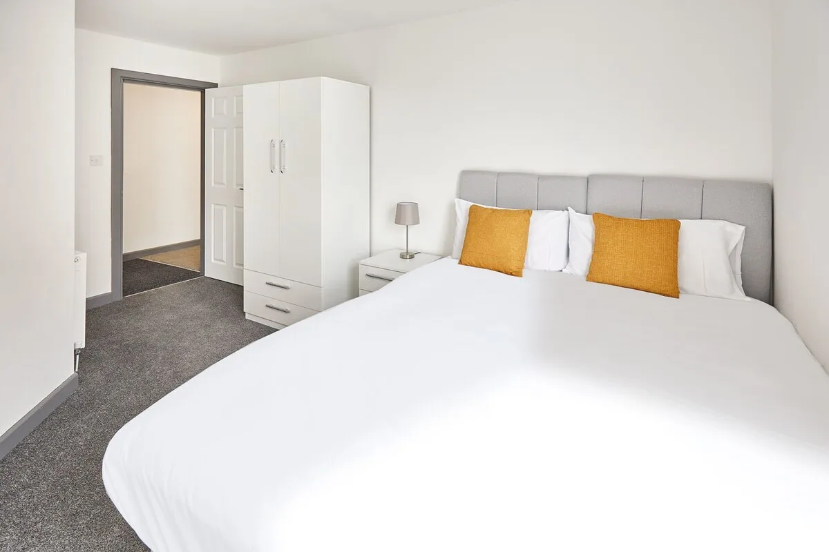 A bright bedroom with a large bed and a white wardrobe beside the doorway.