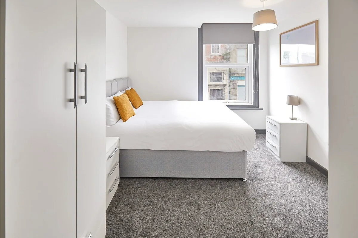 A bright bedroom with a bed, bedside drawers, and a window.