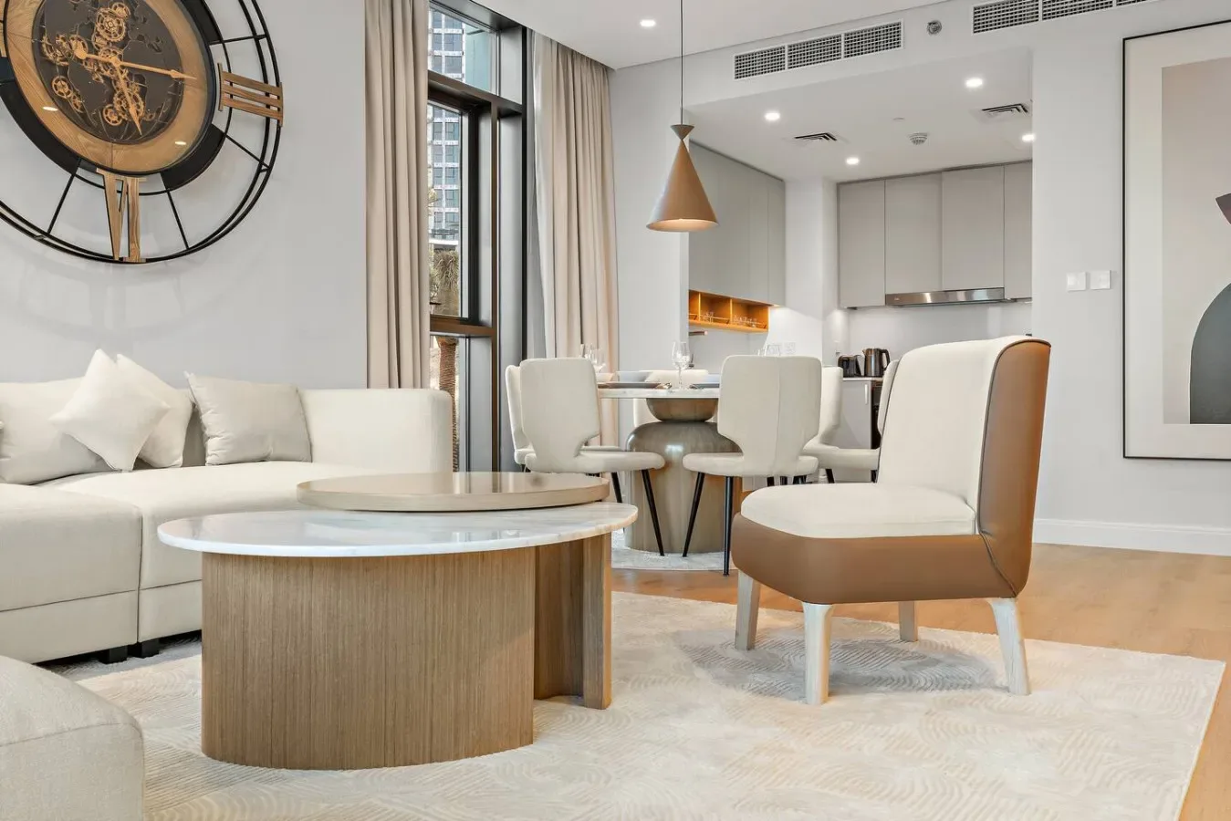 Una luminosa sala de estar y comedor con asientos, una mesa redonda y una cocina al fondo.