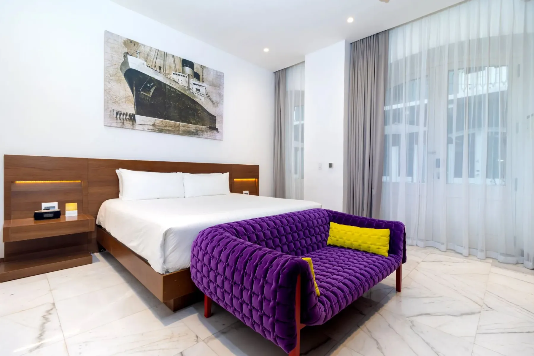 Dormitorio con una cama, un sofá morado y arte en la pared.
