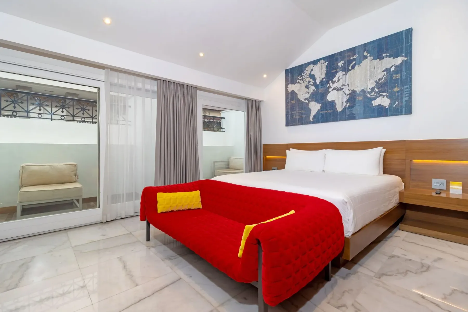 Dormitorio de hotel luminoso con un sofá rojo y acceso a un balcón.
