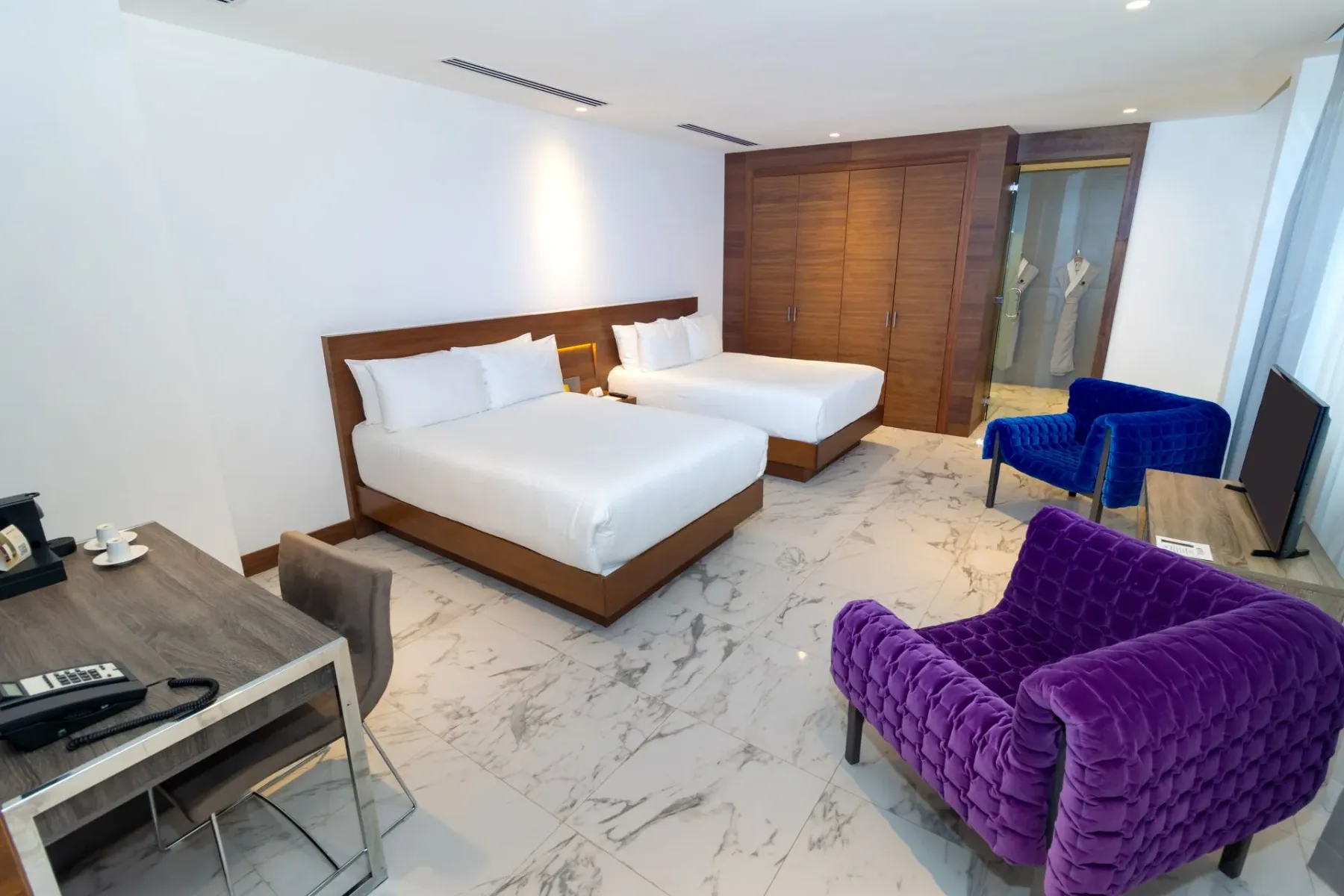 Habitación de hotel con dos camas, un escritorio, sillas y un armario.