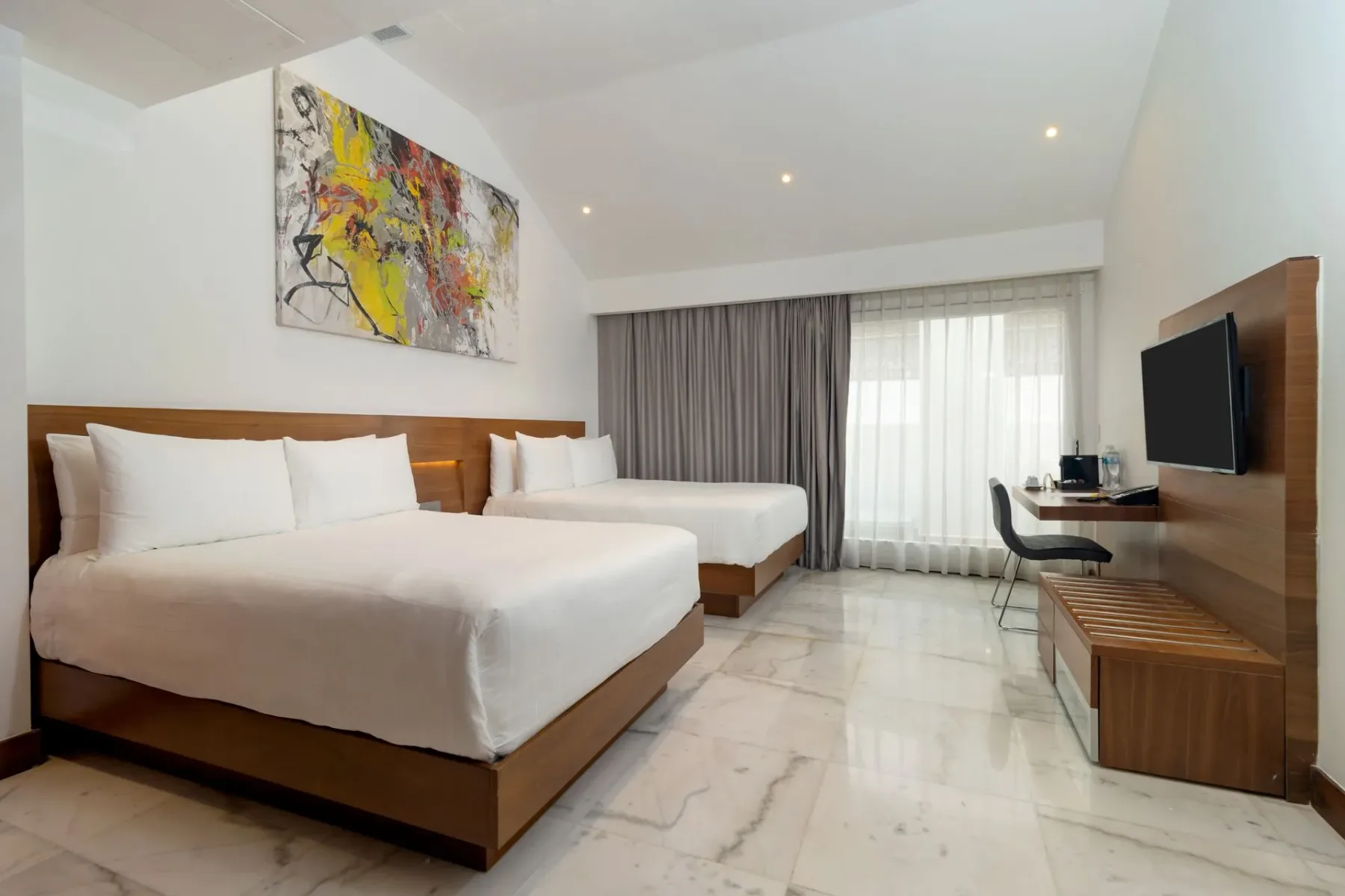 Habitación de hotel con dos camas, un escritorio y arte abstracto en la pared.