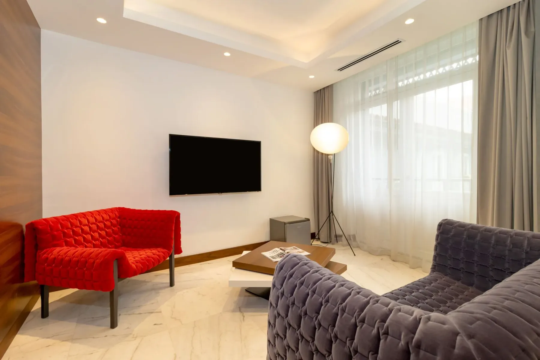 Sala de estar con un sillón rojo, un sofá gris y un televisor.