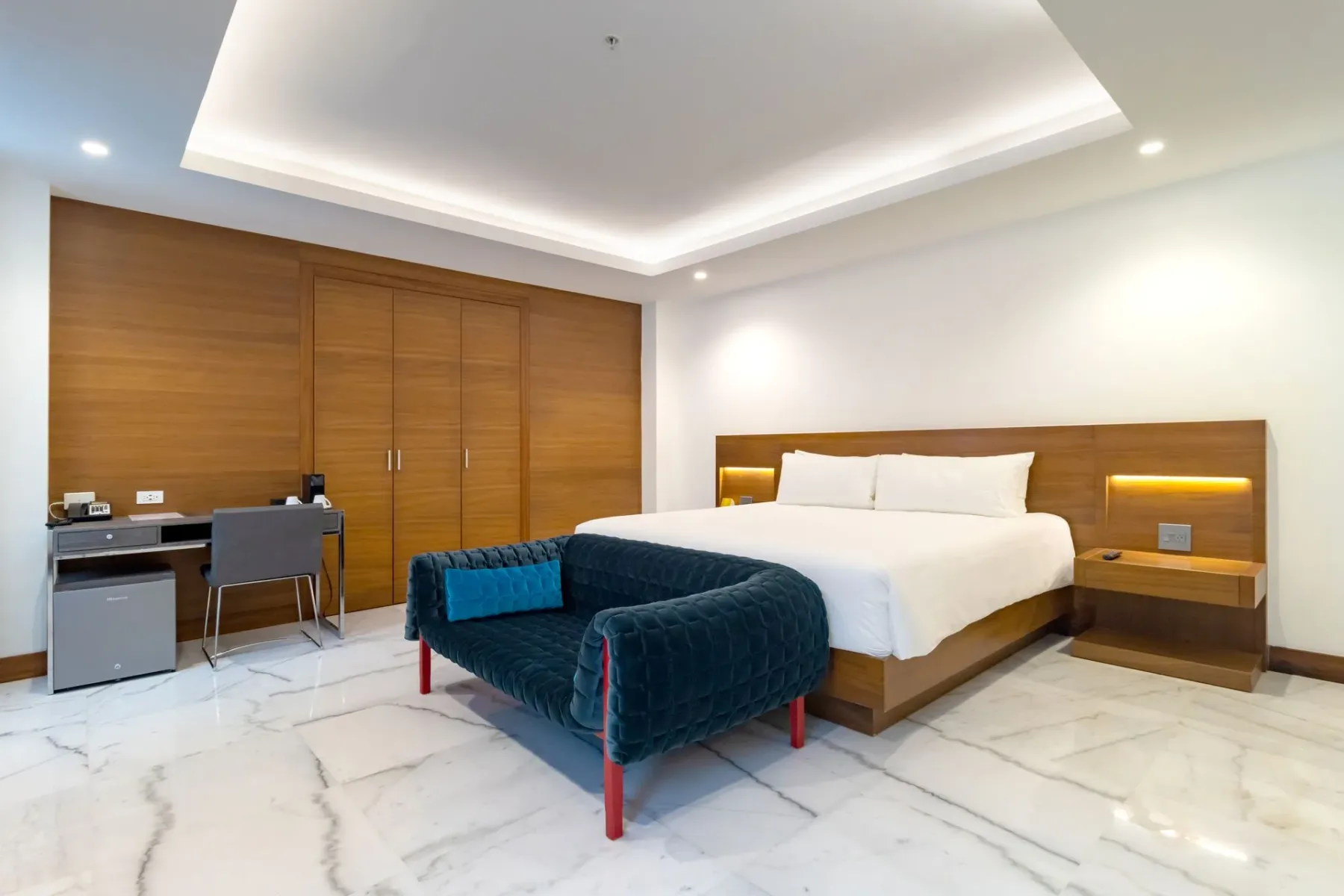 Dormitorio de hotel con una cama, un sofá azul, un armario de madera y un escritorio.