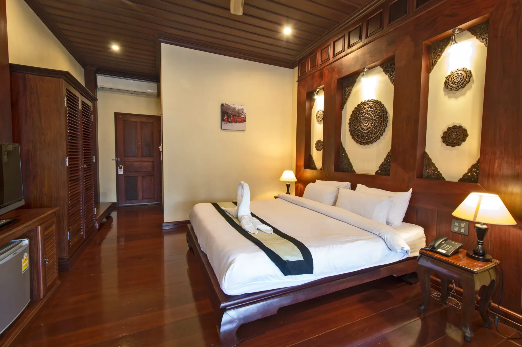 Habitación Deluxe con una cama king, medallones tallados en la pared y suelo de teca pulida.
