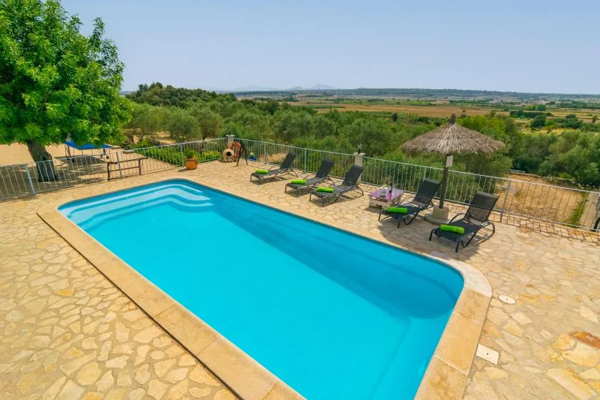 Una piscina al aire libre está junto a una terraza pavimentada con asientos de descanso.