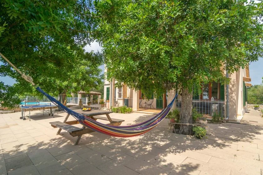 Un patio exterior sombreado con una hamaca bajo árboles frondosos.