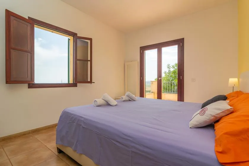 Un dormitorio con una cama grande junto a ventanas abiertas y puertas de vidrio.
