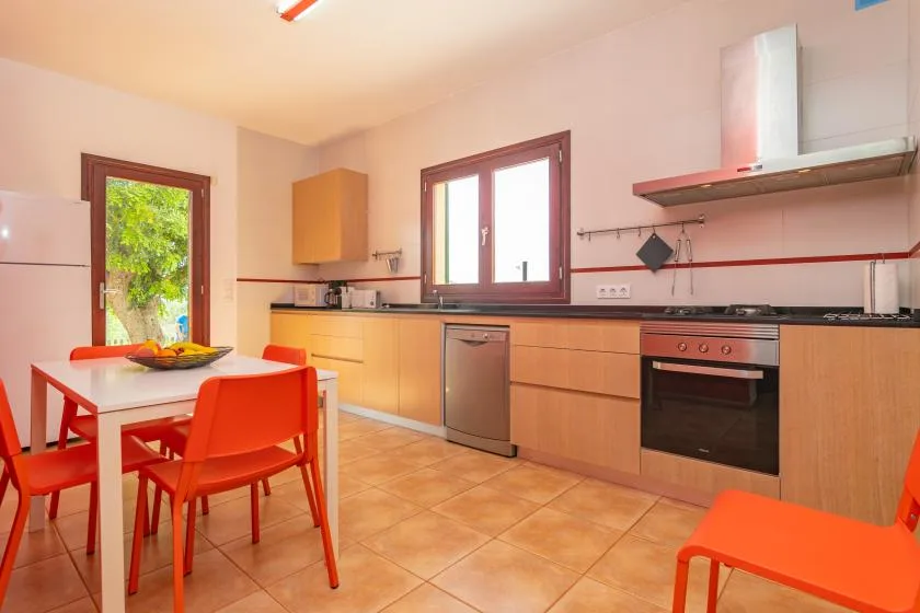 Una cocina luminosa con gabinetes de madera clara, una encimera y una mesa con asientos rojos.