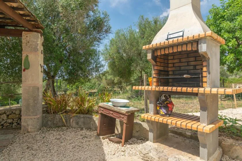 Una barbacoa de ladrillo al aire libre está junto a una mesa pequeña en un jardín frondoso.