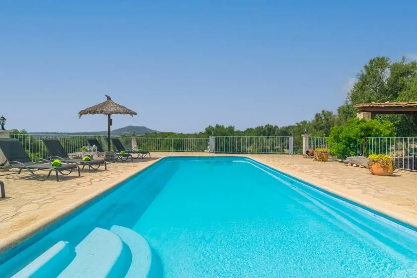 Una piscina al aire libre con asientos reclinables y una sombrilla.