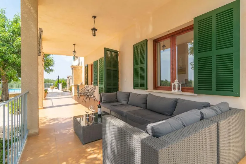 Un patio cubierto con asientos acolchados y contraventanas verdes abiertas.
