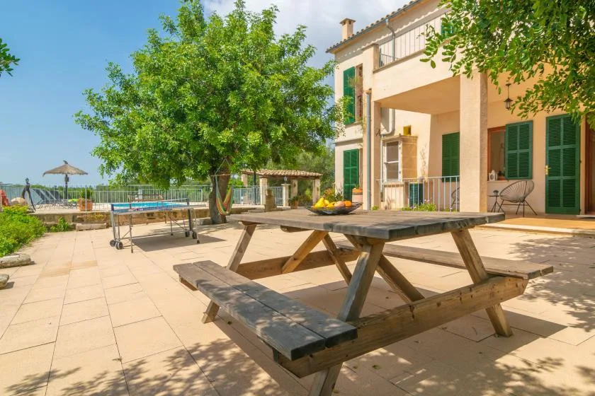 Un patio soleado con una mesa de picnic de madera y una casa.