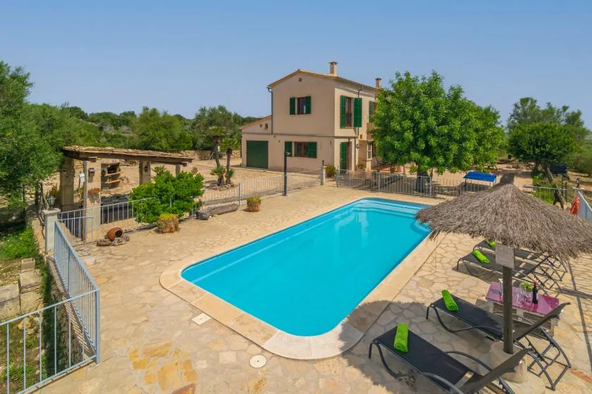 Una piscina junto a una casa de dos plantas, con asientos al aire libre cerca.