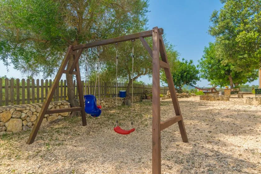 Un columpio al aire libre está bajo árboles frondosos junto a una cerca de madera.