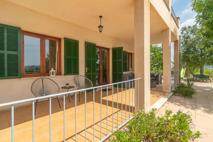Una terraza exterior cubierta con ventanas de contraventanas y asientos junto a un sendero de jardín.