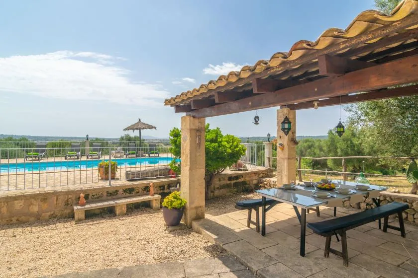 Una zona de comedor exterior a la sombra da a una piscina y al campo circundante.