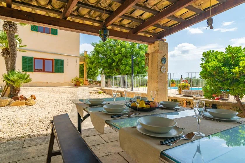 Una zona de comedor exterior a la sombra da a un jardín y una piscina.