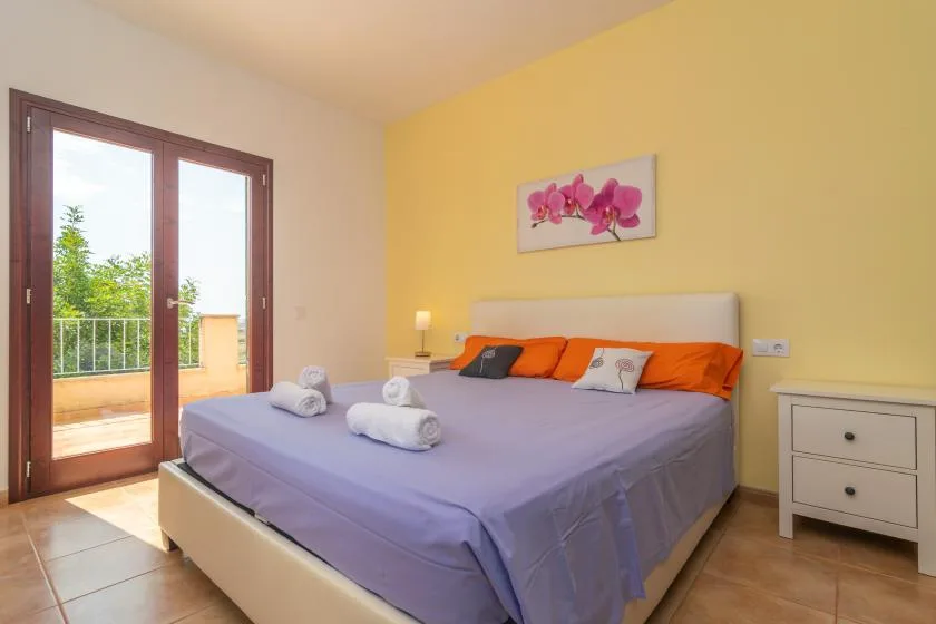 Un dormitorio con una cama grande, almohadas naranjas y puertas de vidrio que dan a un balcón.