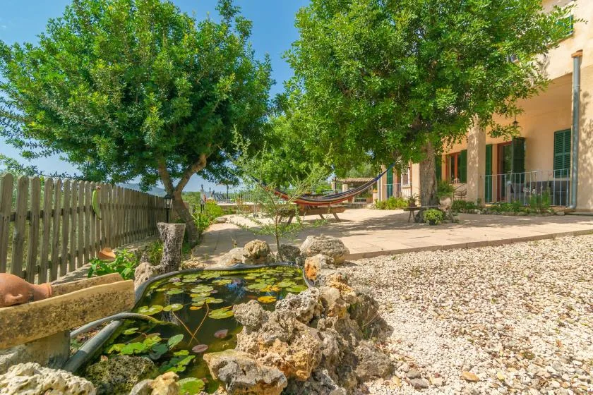 Un patio ajardinado con un pequeño estanque, árboles y una hamaca junto a la casa.