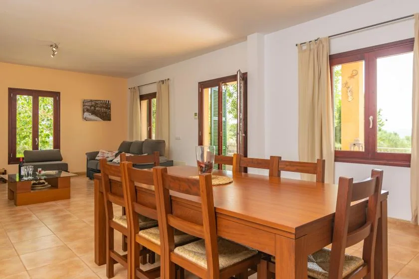 Zona de comedor y estar con una mesa de madera y asientos junto a varias ventanas.