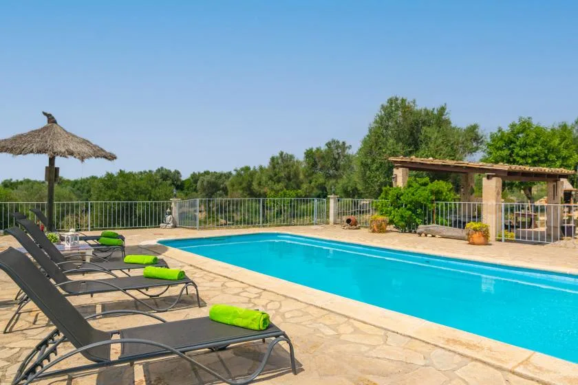 Una piscina al aire libre junto a una terraza pavimentada con asientos reclinables.