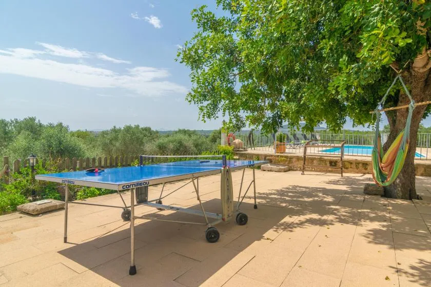 Una mesa de ping-pong está en un patio sombreado junto a una piscina.