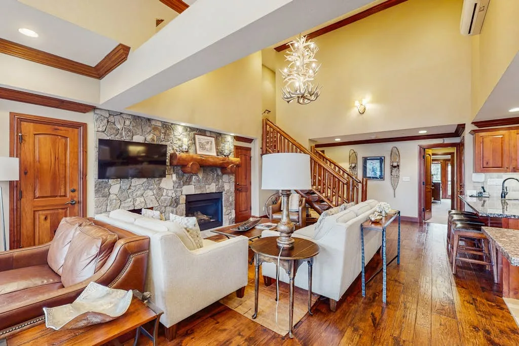 A living room with seating, a stone fireplace, and a staircase.