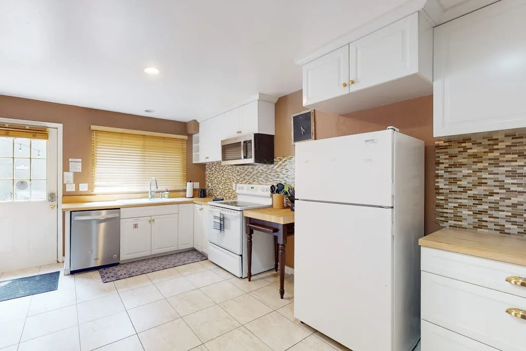A bright kitchen with white cabinets, a refrigerator, and a tiled backsplash.
