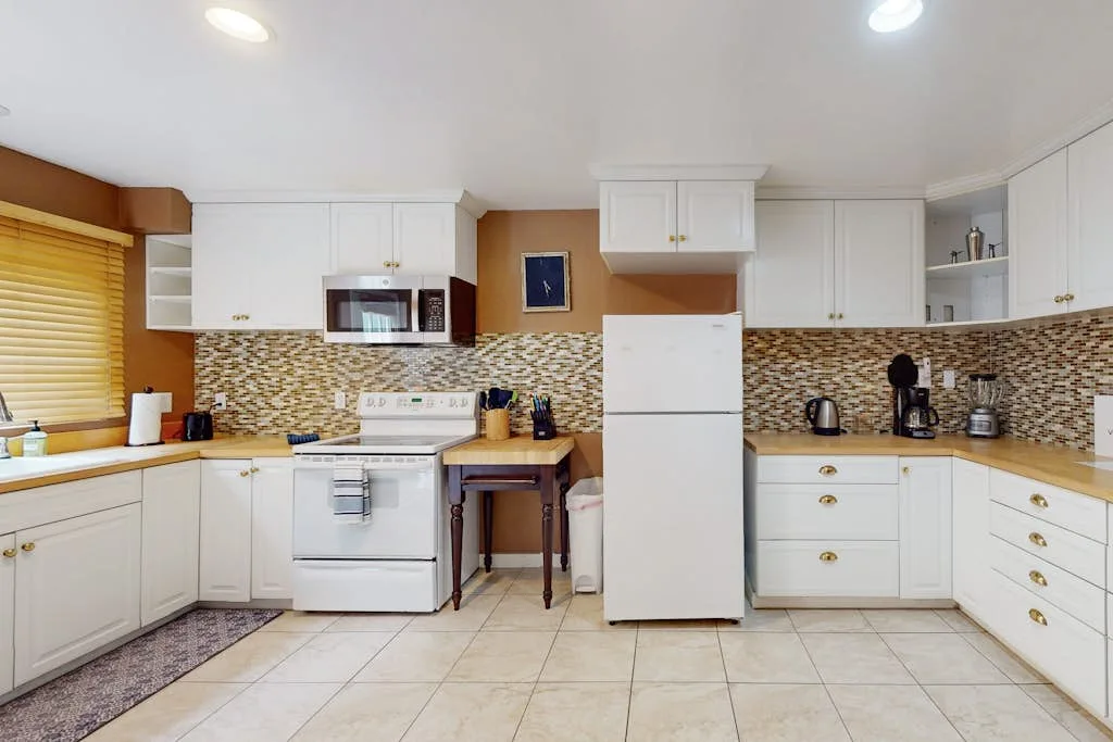 A kitchen with white cabinets, tiled backsplash, and a refrigerator.
