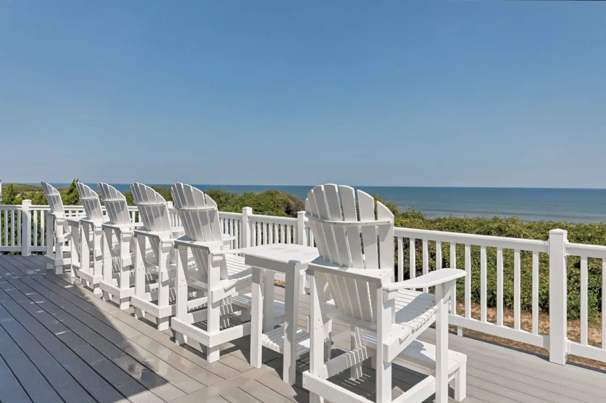 A seaside deck with white chairs and a railing overlooking the water.